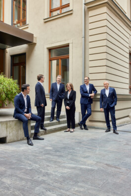 Sechs Menschen in Business-Kleidung stehen und sitzen vor einem Gebäude und unterhalten sich – ein Musterbeispiel für Unternehmensfotografie, die authentische Momente für Unternehmensportraits und Reportagen in Düsseldorf einfängt. Portrait und Reportage Fotografie für Corporate und Editorial