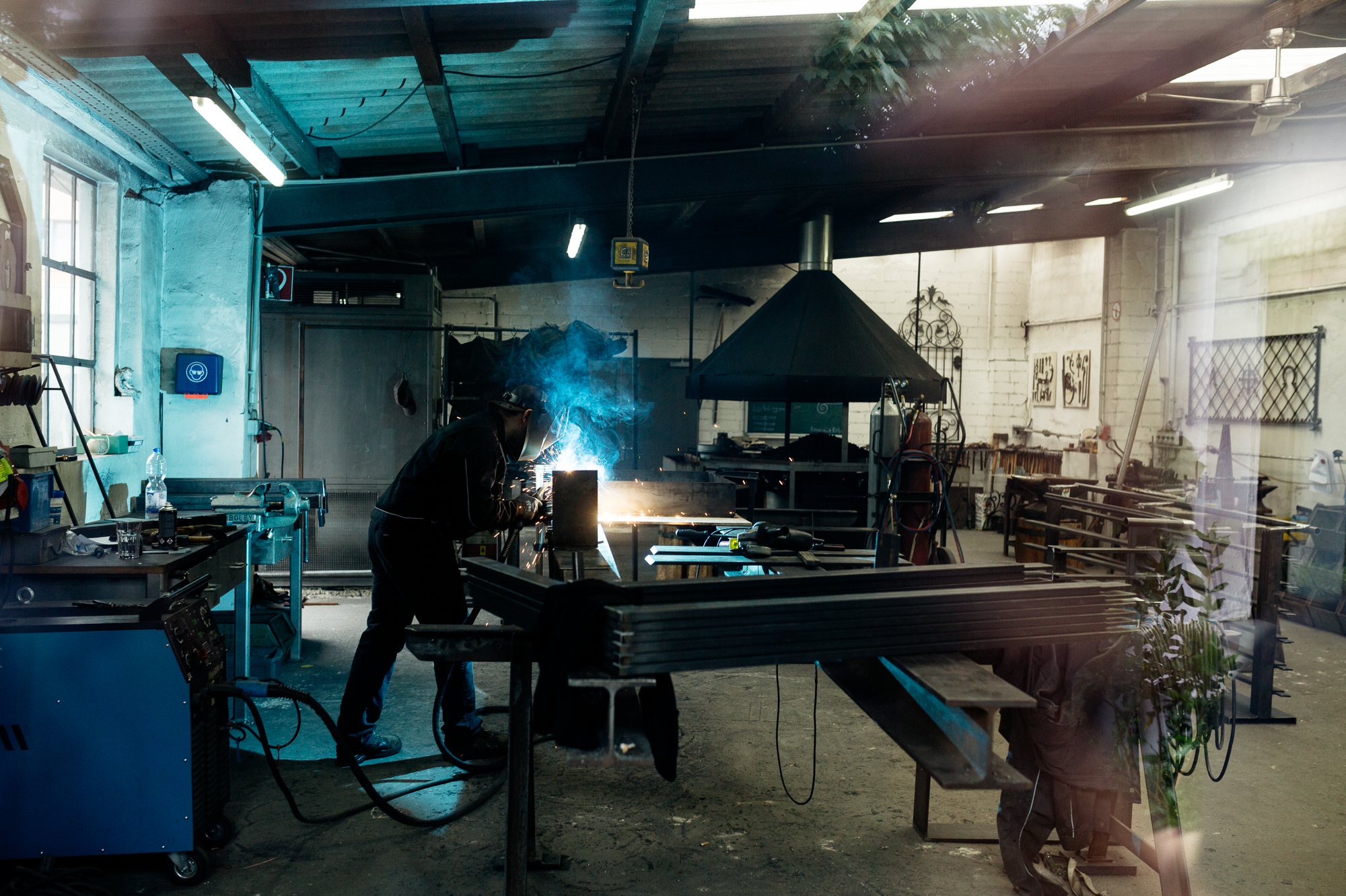 In einer Düsseldorfer Werkstatt sieht man inmitten der hellblauen Schweißfunken eine Person, die in Schutzkleidung gekonnt schweißt. Diese Szene fängt die Essenz der Unternehmensfotografie mit ihrem Fokus auf Industrie und Können ein. Portrait und Reportage Fotografie für Corporate und Editorial