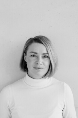 Portraits und Reportagen für Unternehmen: Eine Person mit kurzen Haaren und weißem Rollkragenpullover steht selbstbewusst vor einem schlichten Hintergrund und verkörpert die Essenz der Corporate Fotografie in Düsseldorf. Portrait und Reportage Fotografie für Corporate und Editorial