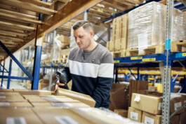 In einem geschäftigen Düsseldorfer Lagerhaus konzentriert sich ein Profi und scannt einen Karton inmitten von Regalen voller verpackter Waren. Diese Szene fängt die Essenz der Unternehmensfotografie ein, bei der Porträts und Reportagen die dynamische Geschichte eines Unternehmens erzählen. Portrait und Reportage Fotografie für Corporate und Editorial