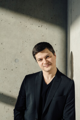 Eine Person im schwarzen Blazer lehnt an einer Betonwand, ihr Schatten wird hinter sie geworfen – ein perfekter Hauch von Corporate Fotografie Düsseldorf, der die Essenz professioneller Eleganz einfängt. Portrait und Reportage Fotografie für Corporate und Editorial