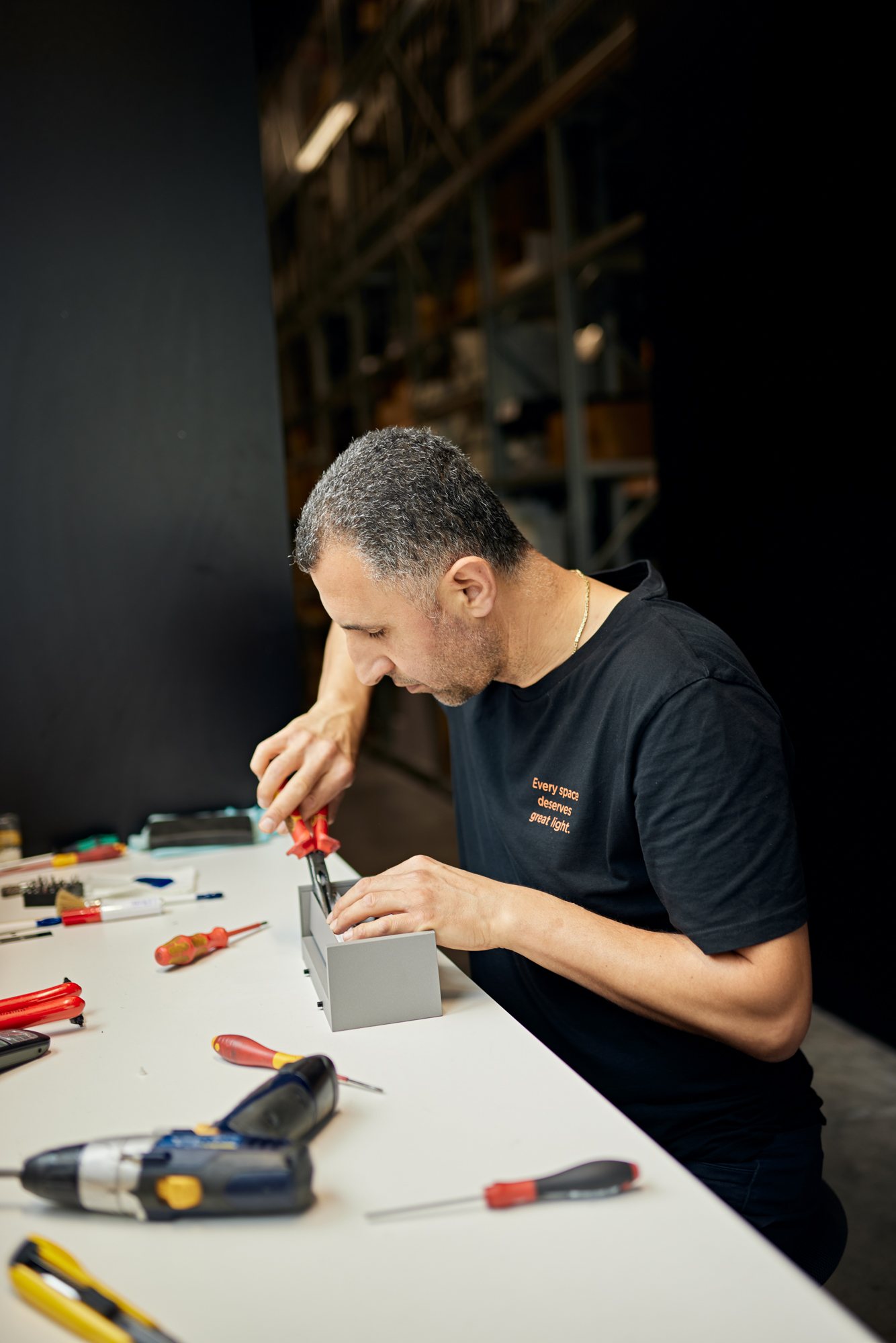 In einer Düsseldorfer Werkstatt sitzt ein Mann an einem Tisch und bedient geschickt einen Schraubenzieher an einem kleinen Gerät, umgeben von einer Reihe von Werkzeugen. Die Szene fängt ein intimes Porträt konzentrierter Handwerkskunst in diesem Unternehmensumfeld ein. Portrait und Reportage Fotografie für Corporate und Editorial