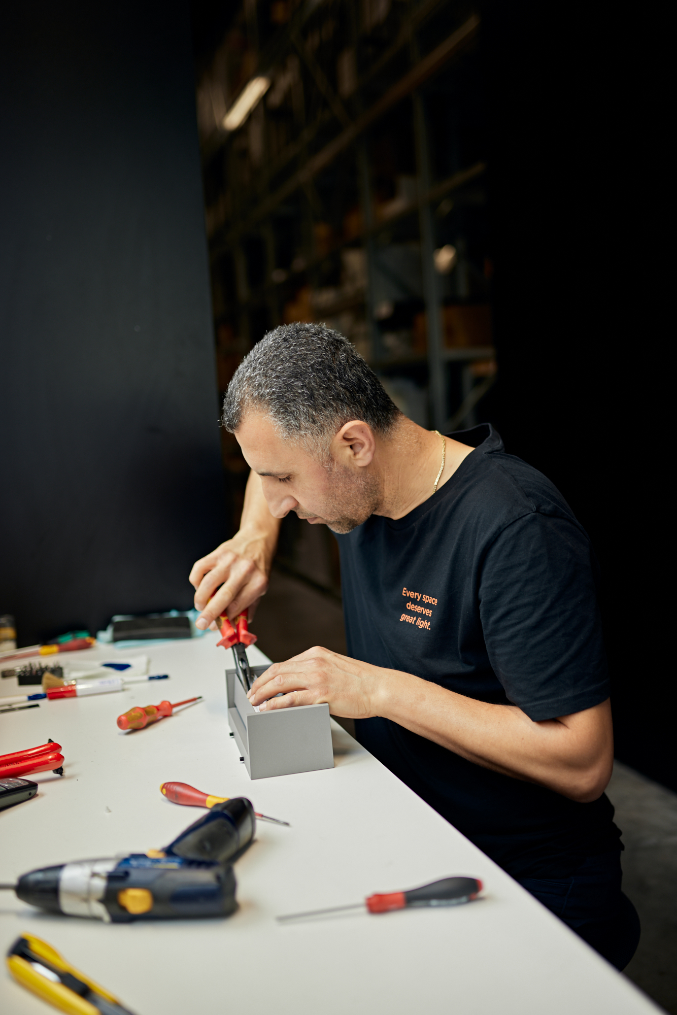 Ein Mann baut fachmännisch ein Gerät am Tisch zusammen, umgeben von einer Vielzahl von Werkzeugen. Die Szene fängt die Essenz von Handwerkskunst und Präzision ein, perfekt für ein Imagefilm-Video, das das Social-Media-Publikum fesseln soll. Portrait und Reportage Fotografie für Corporate und Editorial