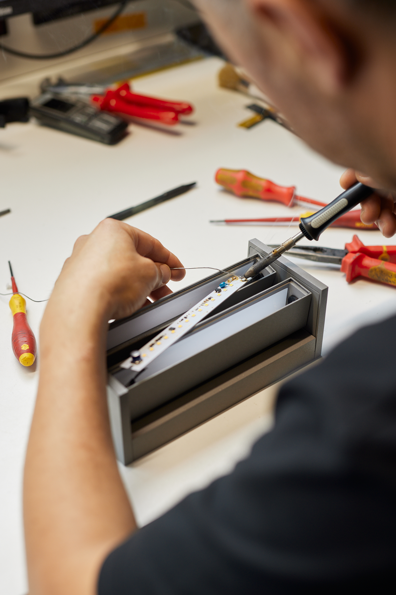 Eine Person lötet sorgfältig Komponenten auf einer Platine, mit Werkzeug und Lötkolben in der Hand, alles festgehalten für einen fesselnden Social Media Imagefilm. Portrait und Reportage Fotografie für Corporate und Editorial