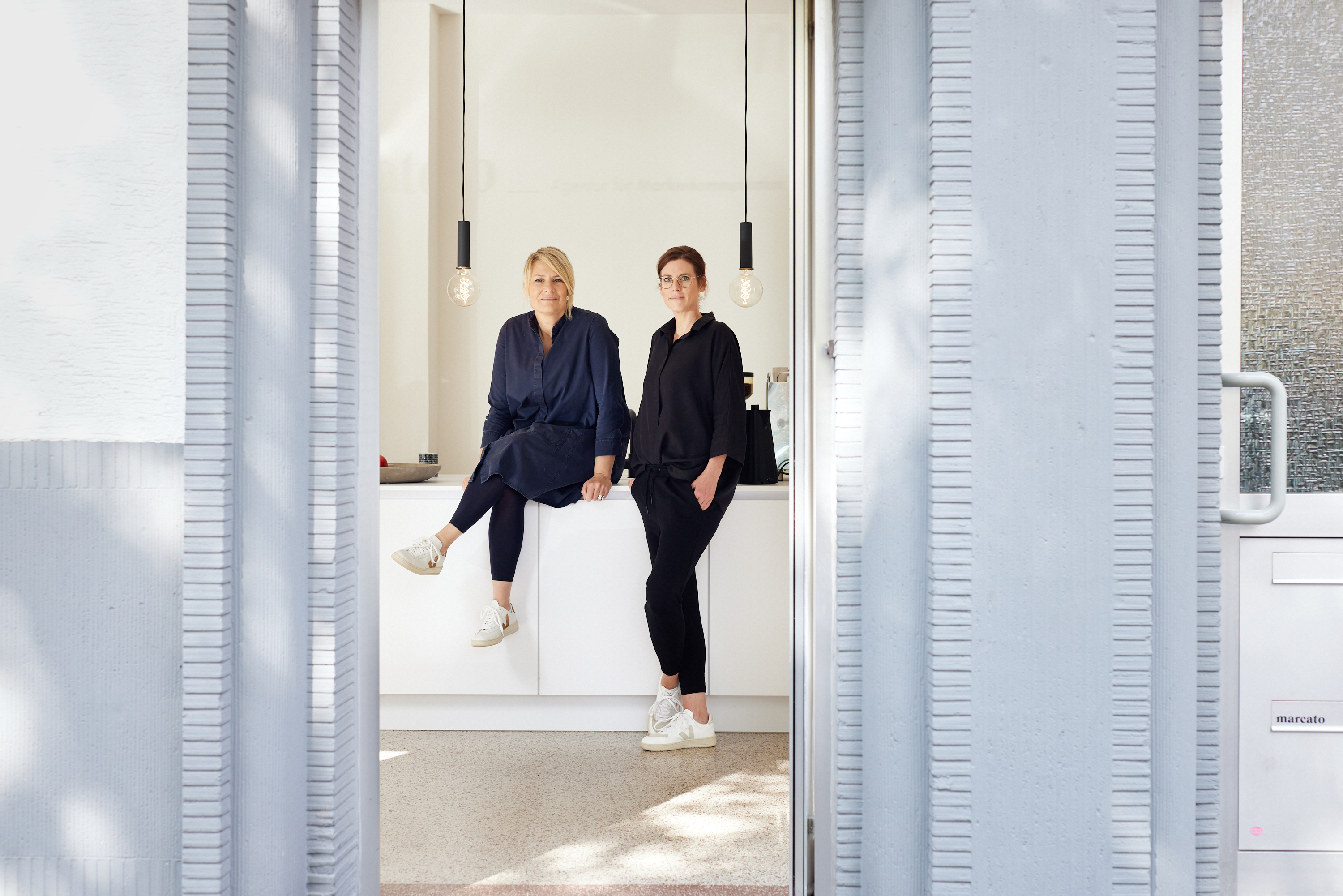 Zwei Frauen, die an einem Tresen sitzen, fangen eine entspannte und doch professionelle Atmosphäre ein - perfekt für ein Geschäftsporträt oder persönliches Branding in einem modernen Unternehmensumfeld. Portrait und Reportage Fotografie für Corporate und Editorial