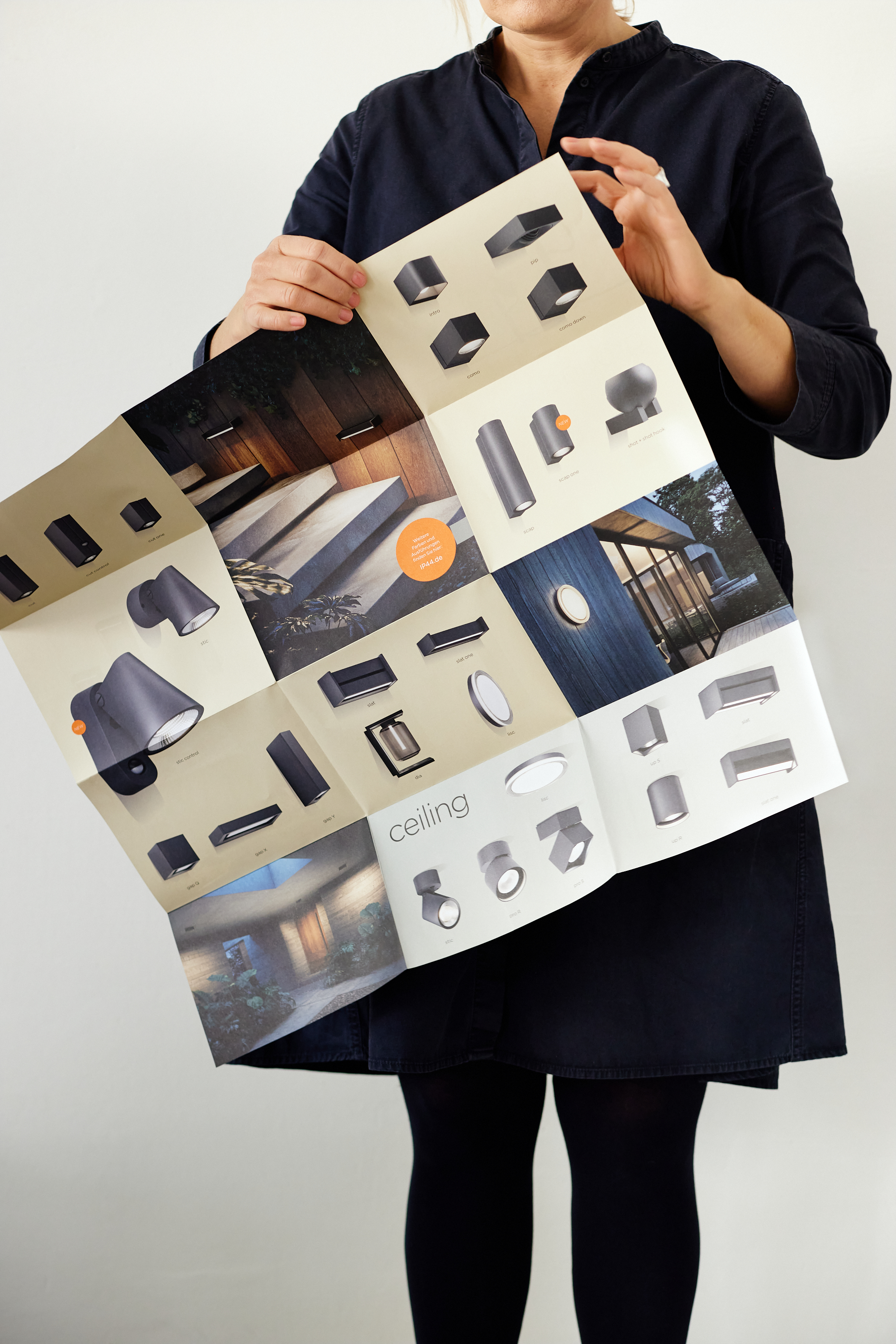 Eine dunkel gekleidete Person hält einen aufgeschlagenen Katalog mit verschiedenen Beleuchtungskörpern und Bildern von installierten Leuchten in der Hand und schafft so ein ausgefeiltes Geschäftsporträt, das sich perfekt für die Markenbildung von Unternehmen oder Privatpersonen eignet. Portrait und Reportage Fotografie für Corporate und Editorial