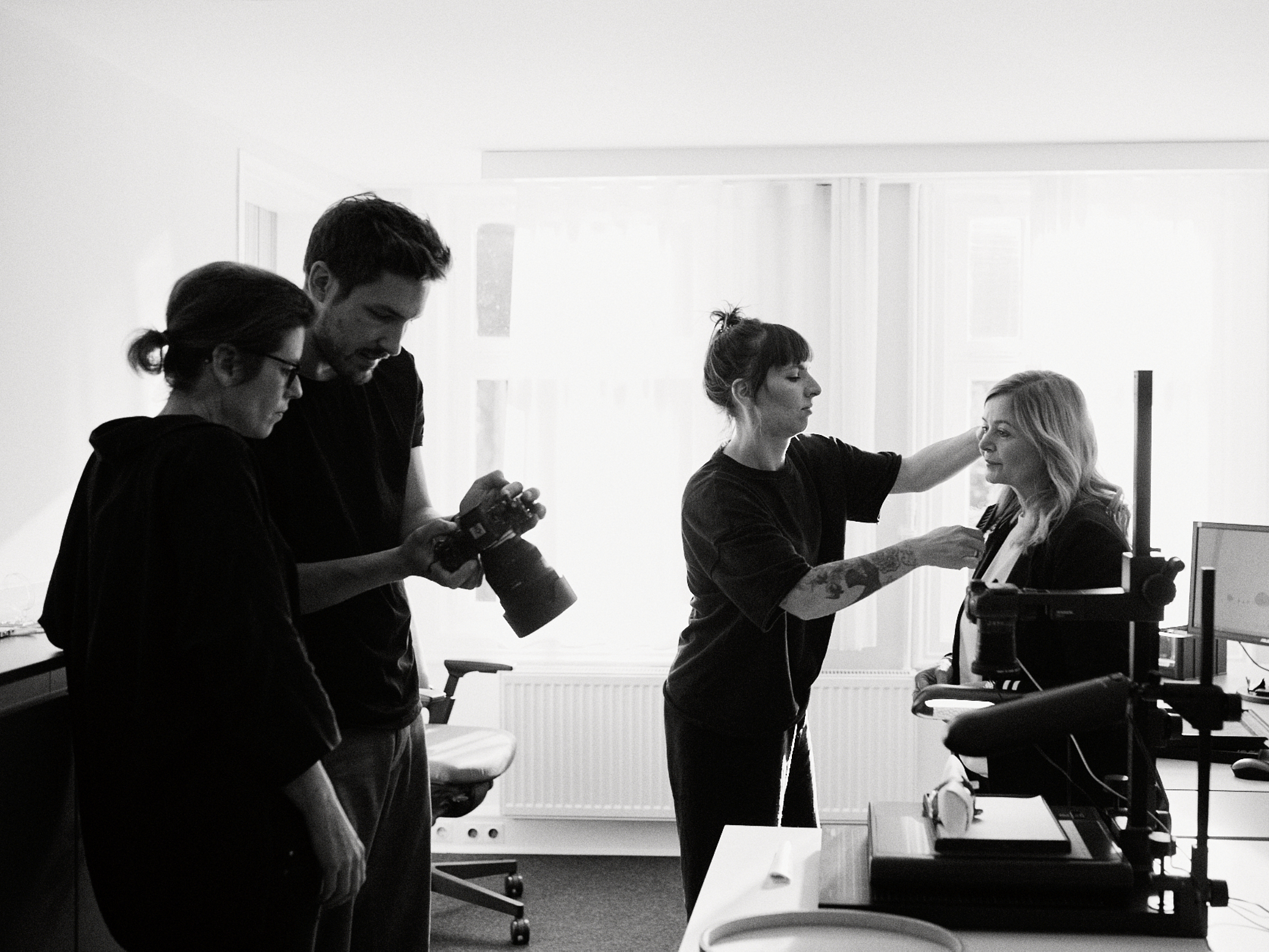 In einem Düsseldorfer Studio entfaltet sich eine authentische Szene, während ein erfahrener Fotograf den Moment einfängt. Eine Person hält die Kamera mit Präzision, während eine andere vorsichtig die Haare einer sitzenden Frau zurechtrückt und so eine Atmosphäre der Kreativität und Zusammenarbeit in der Gruppe schafft. Portrait und Reportage Fotografie für Corporate und Editorial