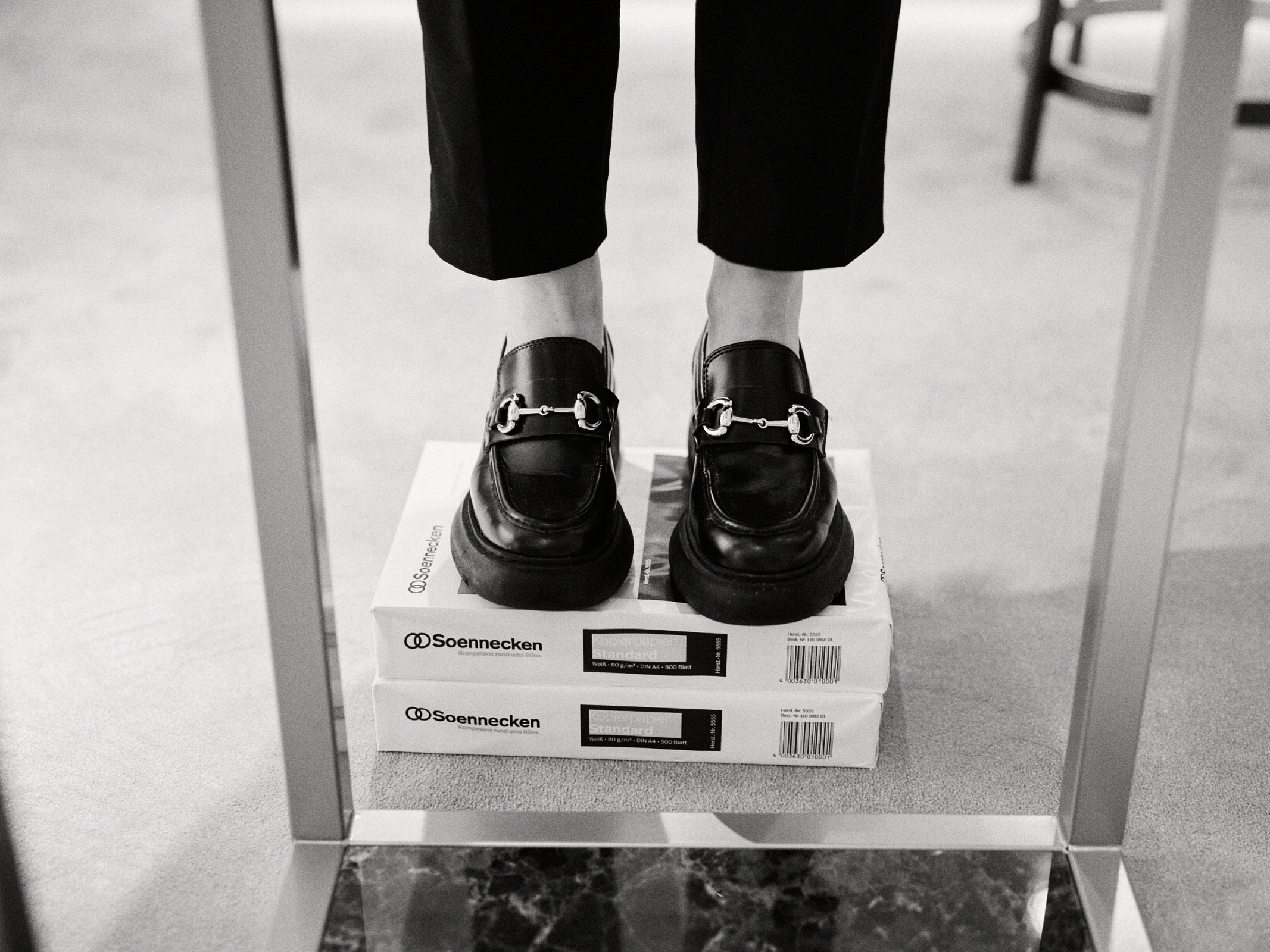 Eine Person steht auf zwei Packungen Druckerpapier vor einem Spiegel, trägt schwarze Slipper und eine dunkle Hose – ein Schnappschuss, der einem Fotografen in Düsseldorf, NRW, vielleicht Interesse wecken könnte. Portrait und Reportage Fotografie für Corporate und Editorial