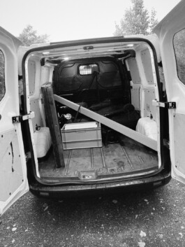 Geöffnete Türen des Lieferwagens geben den Blick auf einen teilweise beladenen Laderaum mit einem großen Holzbrett, einem Werkzeugkasten und anderen Materialien frei und erfassen so eine authentische Szene, die an den Blick hinter die Kulissen eines Düsseldorfer Fotografen erinnert. Portrait und Reportage Fotografie für Corporate und Editorial