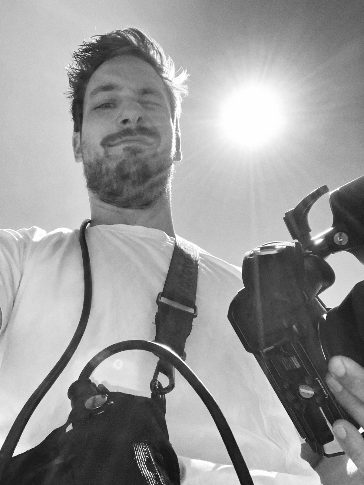 Eine Person im weißen Hemd, die einen authentischen Stil verkörpert, hält eine Kamera und blickt in die Sonne, wodurch faszinierende Lichtreflexe entstehen. Portrait und Reportage Fotografie für Corporate und Editorial