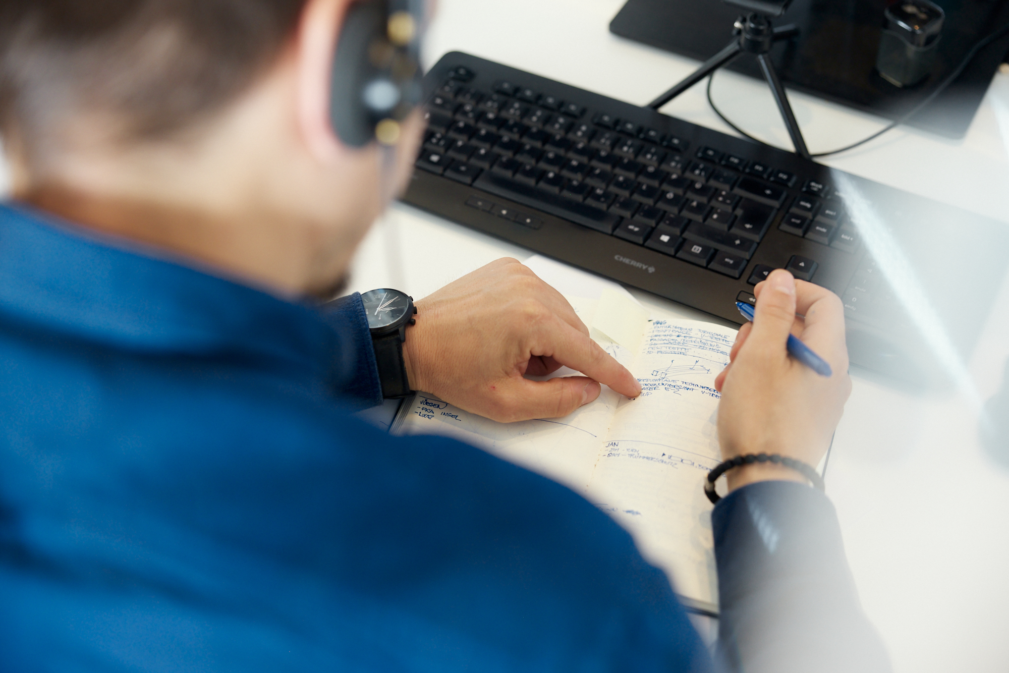 Eine Person mit Headset blickt auf ein Notebook und zeigt mit dem Finger darauf, im Hintergrund ist eine Tastatur zu sehen, und fängt einen für Unternehmensfotografie geeigneten Moment ein. Portrait und Reportage Fotografie für Corporate und Editorial