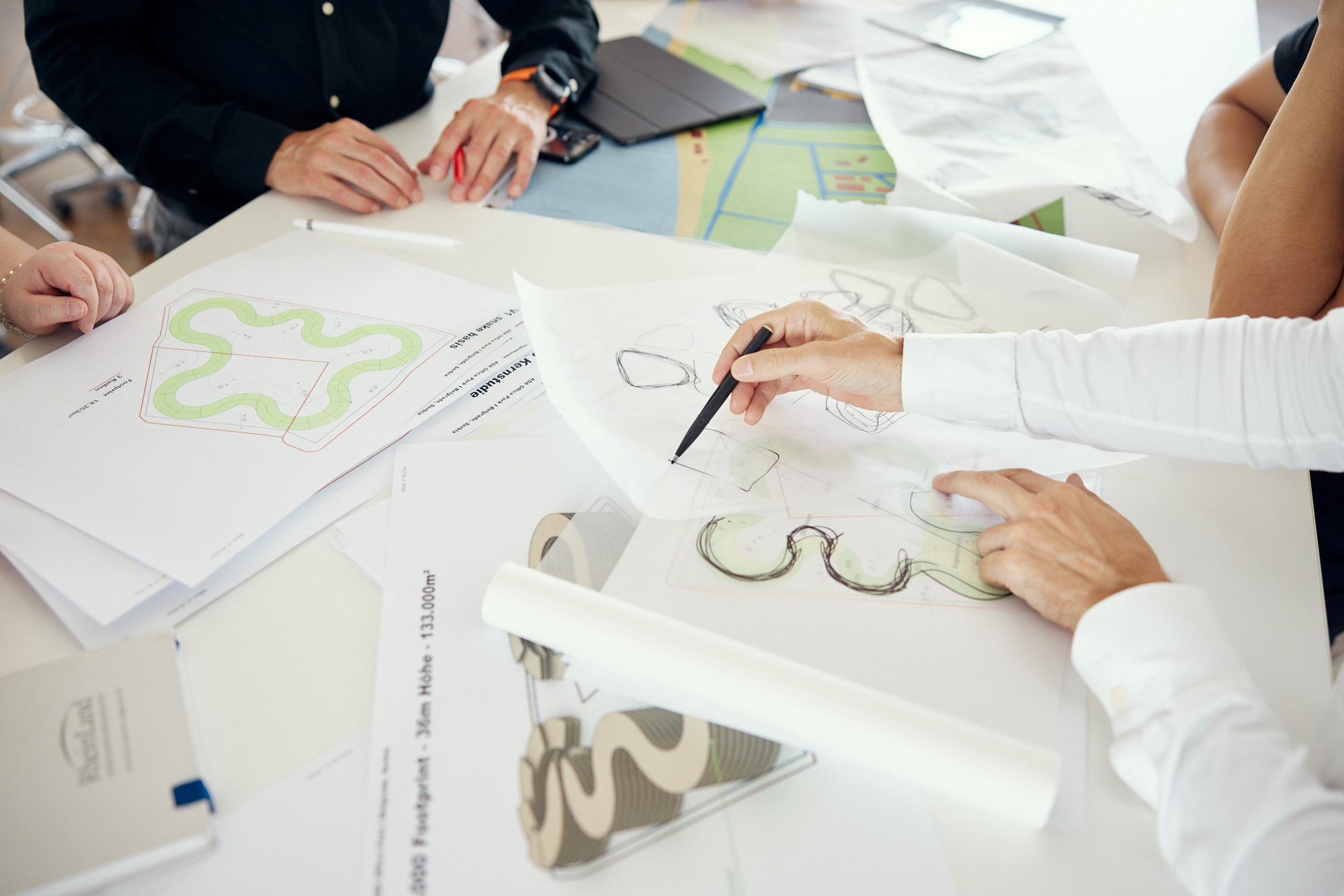 Menschen versammelten sich authentisch um einen Tisch und diskutierten leidenschaftlich über Architekturpläne und Skizzen, einige hielten Stifte und Papier in der Hand. Die Szene fängt die Essenz der Unternehmensfotografie ein, wo Zusammenarbeit auf Kreativität trifft. Portrait und Reportage Fotografie für Corporate und Editorial